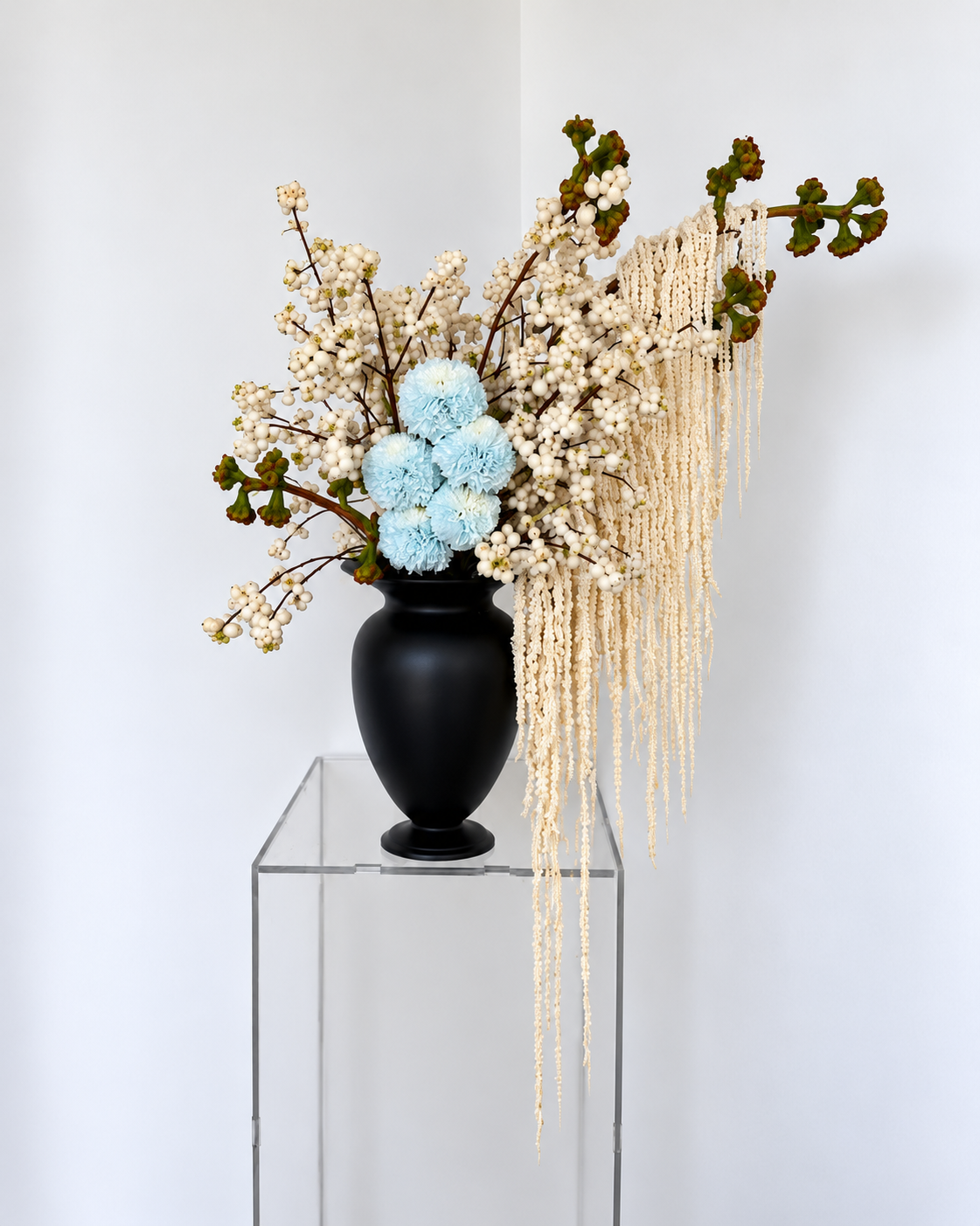 Composition bleu pâle et blanche dans un vase noir avec amarantes retombantes