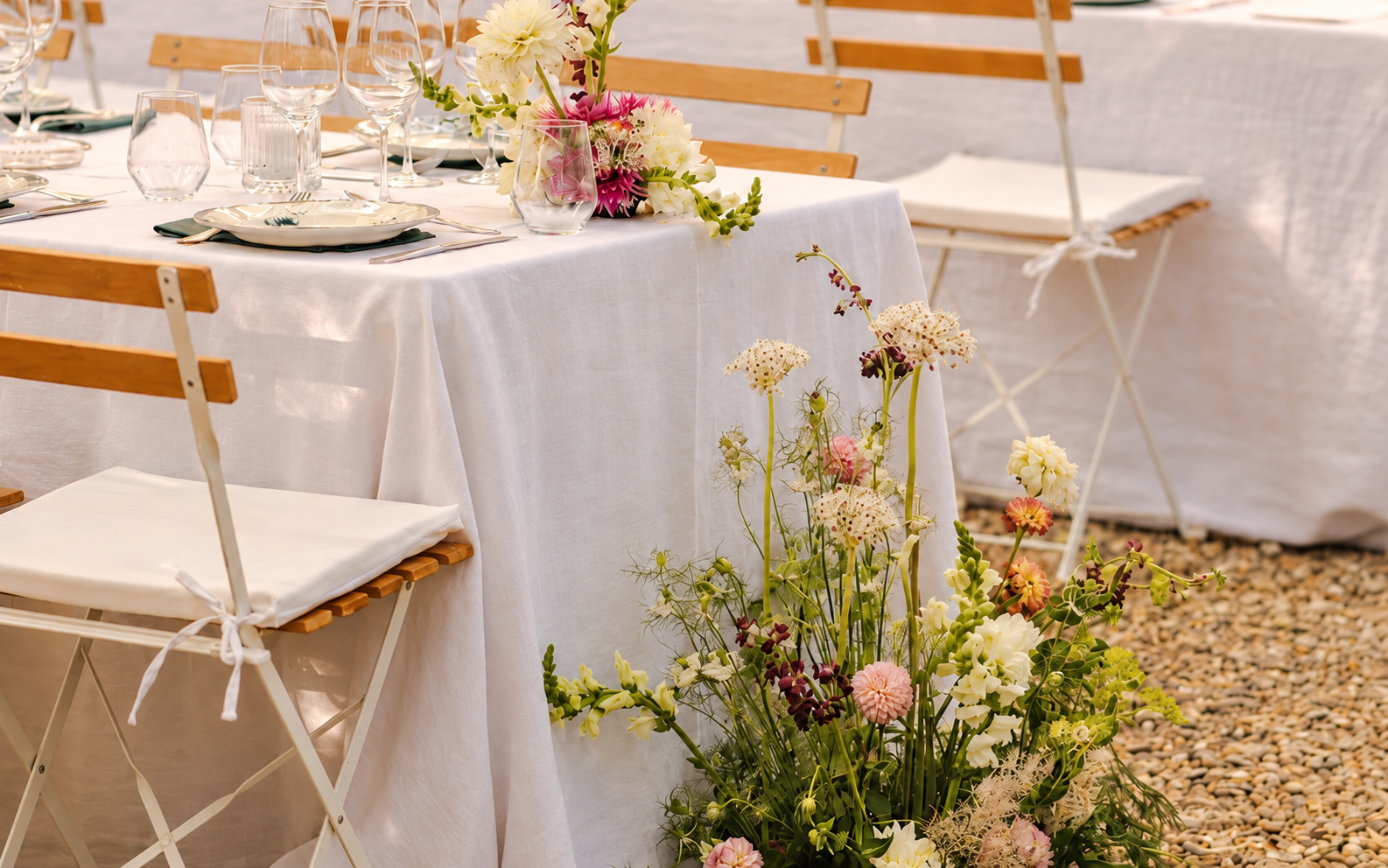 Fleurs de cérémonie claires au pied d’une table habillée de blanc, en extérieur