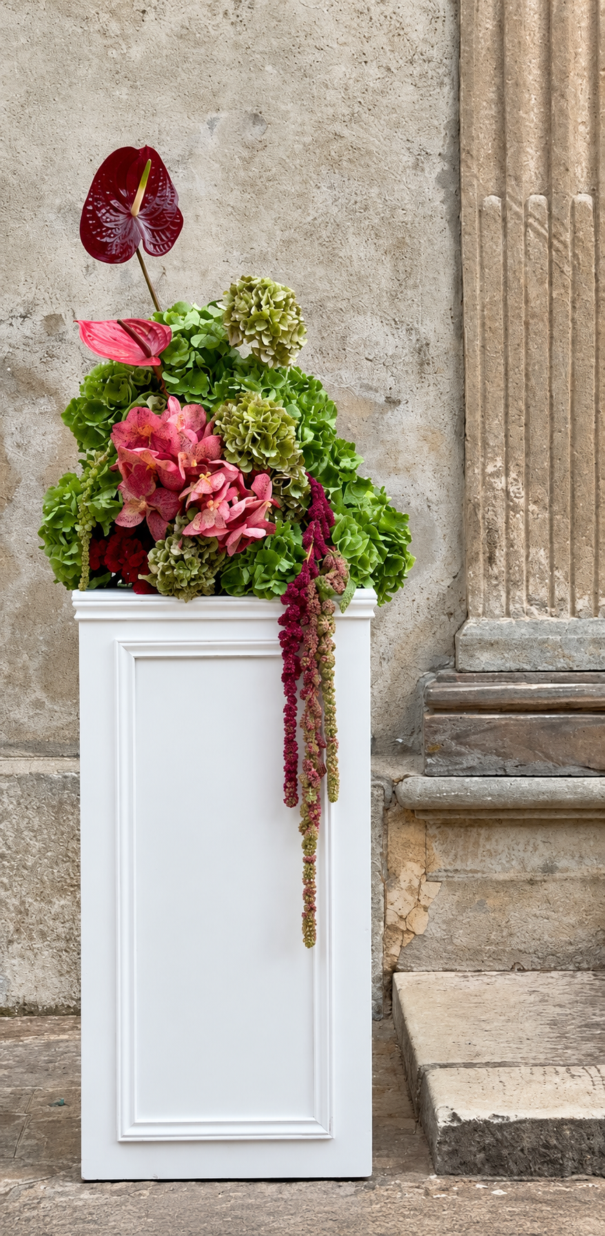 Composition rose et verte avec un anthurium, sur une colonne de pierre