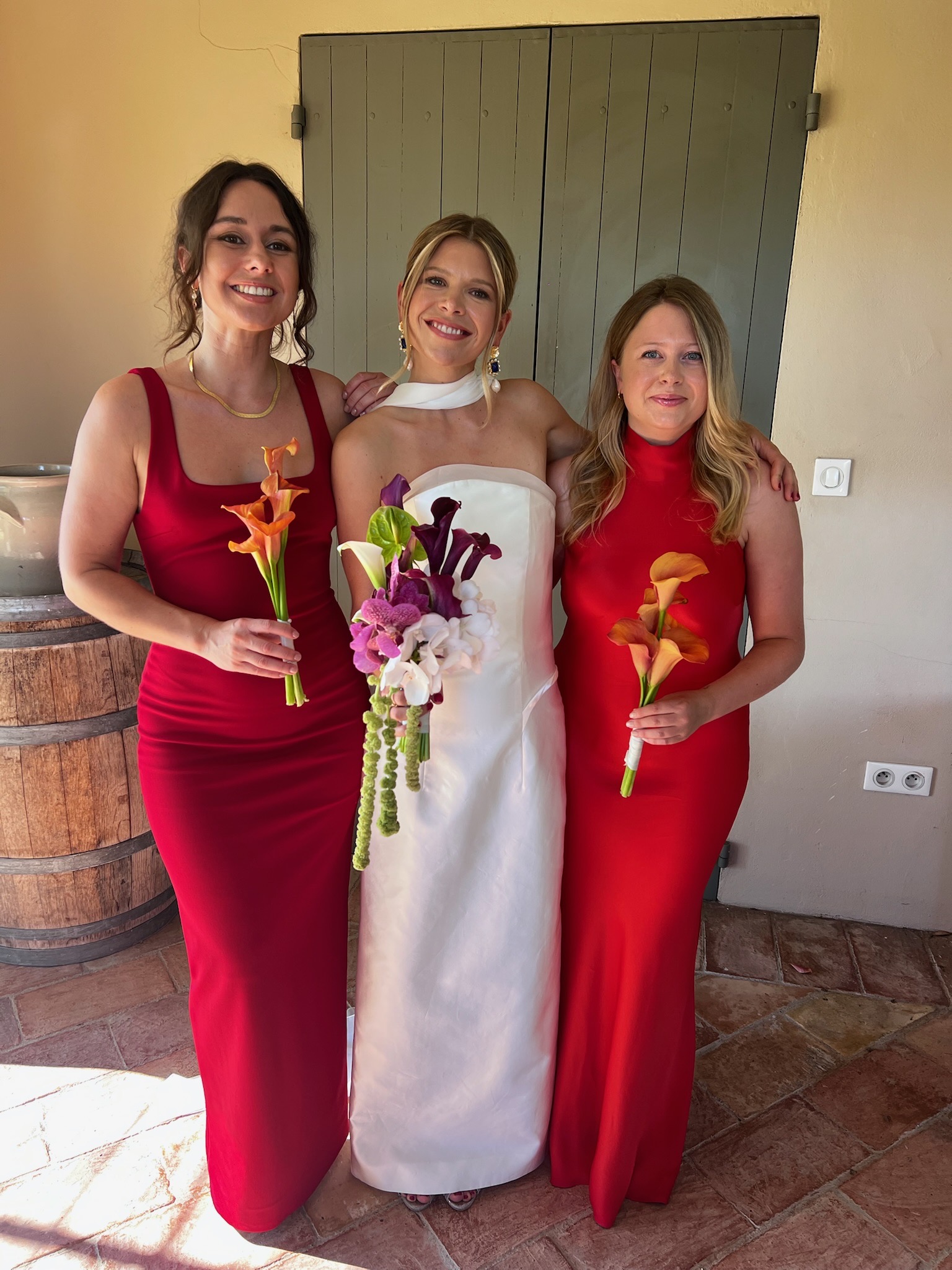 La mariée en blanc entourée de deux femmes en robes rouges, chacune tenant un bouquet
