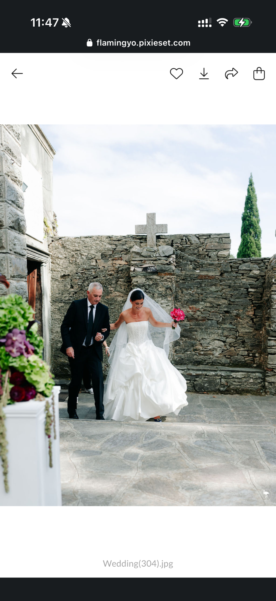 La mariée avec son bouquet rose devant une église en pierre et une composition fleurie