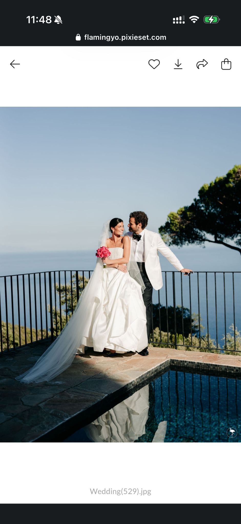 Les mariés avec un bouquet rose au bord de la piscine, face à la mer